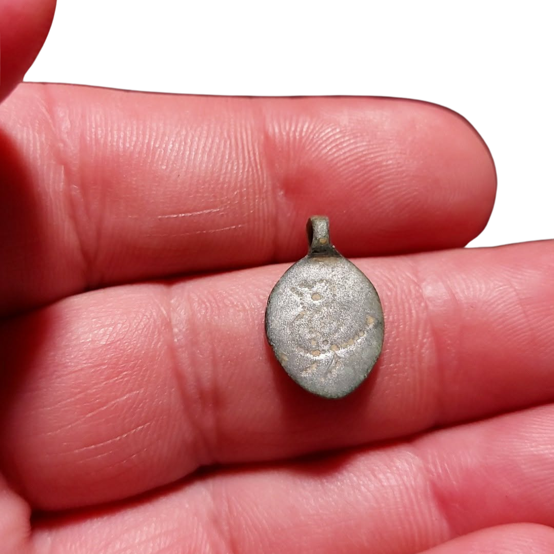 A small oval silver pendant with a loop at the top, resting on a person's fingers against a white background.