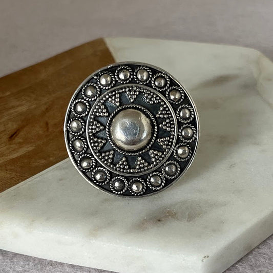 Silver ring with intricate design on a marble surface